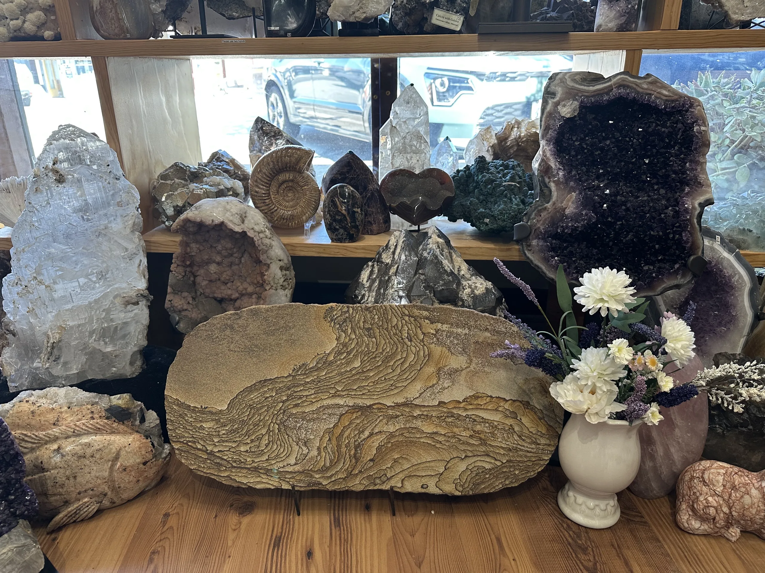 Window display with large amethyst geode, fossil slab and flowers